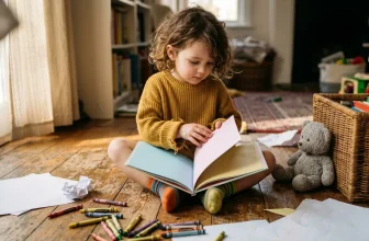 Petite fille en pull jaune lisant un livre coloré assis par terre